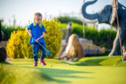 Young boy playing crazy golf with ear defenders around her neck